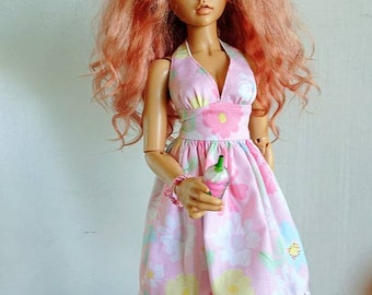May include: A doll with long, curly, pink hair wearing a pink and white floral halter dress with a white lace trim. The doll has green eyes and is holding a small green and white object.