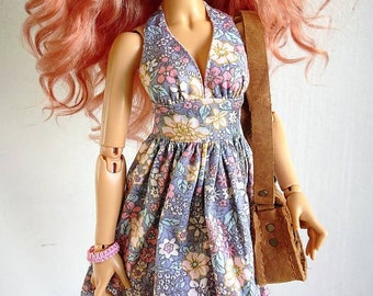 May include: A doll with long, curly, pink hair wearing a floral print dress with a brown leather strap bag.