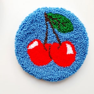 May include: A blue circular rug with a red cherry design. The cherries have green stems and leaves.