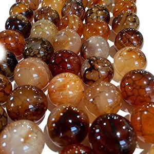 Puede incluir: Primer plano de una colección de cuentas redondas y pulidas de piedras preciosas en tonos marrón, ámbar y negro. Las cuentas tienen un acabado brillante y patrones variados, adecuadas para la fabricación de joyas o manualidades.