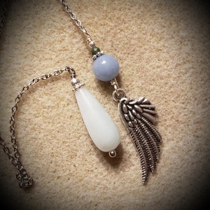 May include: Two silver dowsing pendulums with chains. One pendulum has a white teardrop-shaped crystal and the other has a light blue round crystal with a silver angel wing charm.