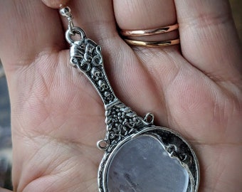 May include: A silver necklace with a crescent moon pendant featuring a clear crystal. The pendant has an ornate design with floral details. The necklace also includes a pink gemstone bead.