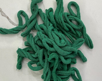 May include: A pile of bright green knitted rope, with a twisted design. The rope is thick and appears to be made of a soft, textured material. The loops and twists create a visually interesting pattern. The rope is scattered on a white surface.
