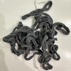May include: A tangled pile of gray rope, likely for crafting or general use. The rope is thick and appears to be made of a woven material. The loops and knots suggest it's been used or prepared for a project.
