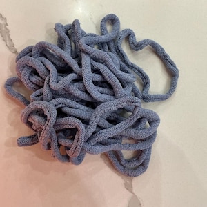 May include: A tangled bundle of blue-gray knitted cord. The cord appears to be made of a soft, textured material, and is looped and intertwined. The image is taken from a close-up perspective, highlighting the texture and color of the cord.