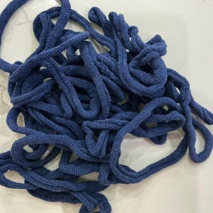 May include: A tangled pile of navy blue knitted rope. The rope appears to be made of a soft, textured material. The image is a close-up shot, highlighting the details of the rope's construction and color.