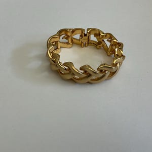 May include: A gold-colored bracelet with a chain-link design. The bracelet is made of metal and has a shiny finish. The links are interlocked, forming a continuous loop. The bracelet is a piece of jewelry.