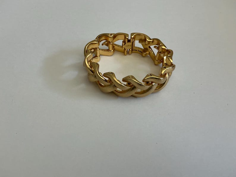 May include: A gold-colored bracelet with a chain-link design. The bracelet is made of metal and has a shiny finish. The links are interlocked, forming a continuous loop. The bracelet is a piece of jewelry.