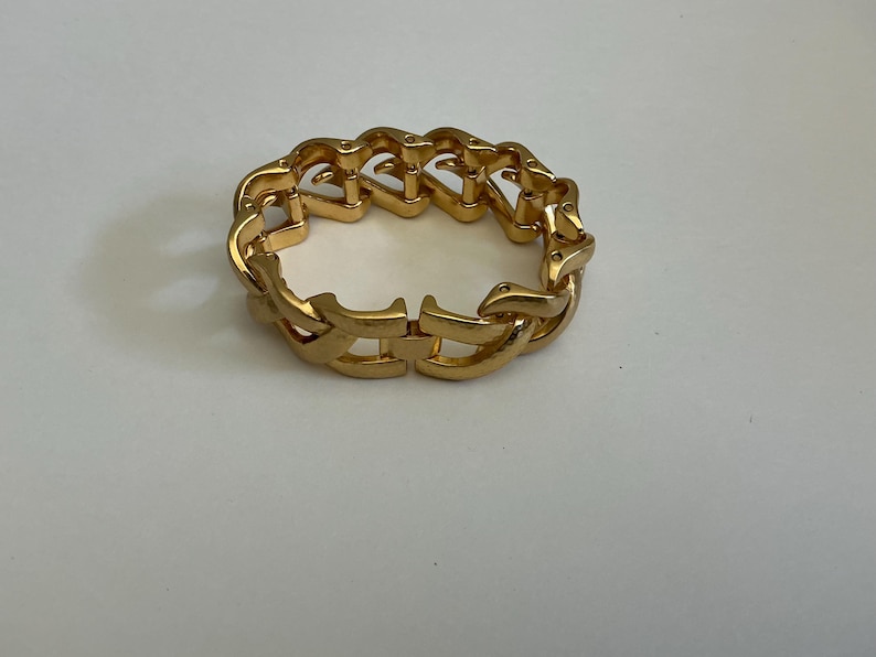 May include: A gold-colored bracelet with a chain-link design. The bracelet is made of metal and has a clasp closure. The links are shaped in a repeating pattern.