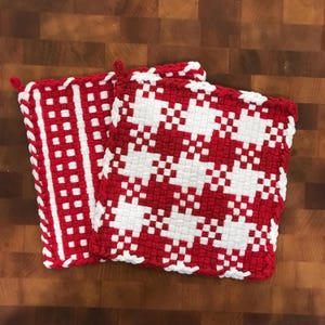 May include: Two red and white woven pot holders with a geometric pattern. The pot holders have a fringe border.