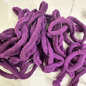 May include: A pile of thick, knitted purple rope. The rope is a vibrant shade of purple, with a textured surface. The rope is looped and coiled, creating a tangled appearance. The material appears to be soft and flexible.