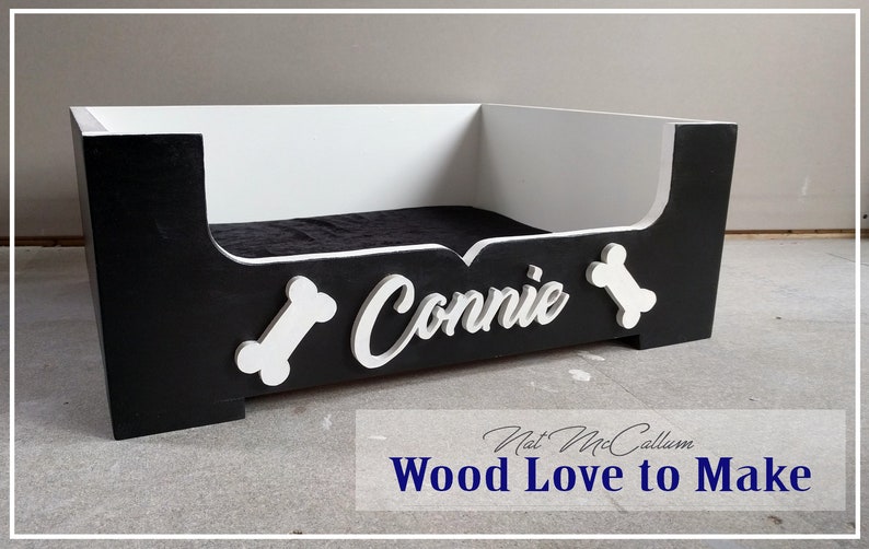 Puede incluir: Cama de perro de madera negra y blanca con el nombre "Connie" y formas de hueso en la parte delantera.