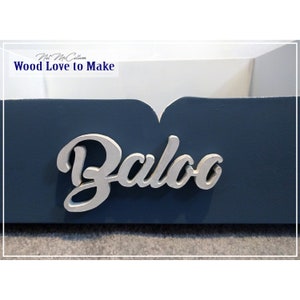 Puede incluir: Una caja de madera azul con un interior pintado de blanco. La caja tiene una placa de nombre de madera pintada de plata que dice "Baloo". La caja est&aacute; etiquetada como "Nat McCallum Wood Love to Make".