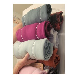 May include: A stack of rolled up clothing in a closet. The clothing is in various colors, including teal, pink, light blue, orange, and white. The clothing is folded and rolled up, and then tied with a white string.