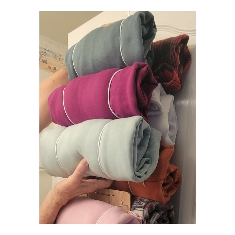 May include: A stack of rolled up clothing in a closet. The clothing is in various colors, including teal, pink, light blue, orange, and white. The clothing is folded and rolled up, and then tied with a white string.