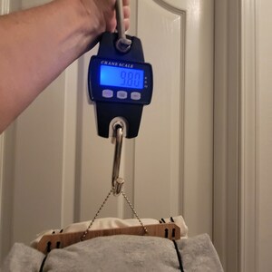 May include: A black digital crane scale with a hook hanging a gray and white blanket. The scale reads 9.80.