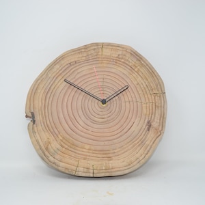 May include: A round wooden clock with black hands and a light brown wood grain pattern. The clock face is made from a tree trunk slice, showing the rings of the tree.
