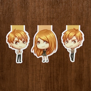 Puede incluir: Tres marcapáginas de personajes de dibujos animados con pelo naranja y ojos grandes. Dos son personajes masculinos con trajes y uno es un personaje femenino con uniforme escolar. Los marcapáginas tienen un borde blanco y una pestaña beige.