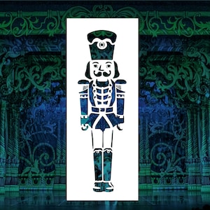 May include: White stencil of a Nutcracker soldier in a blue and white uniform with a red sash and a black hat. The stencil is on a blue and green background.
