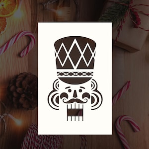 May include: A black and white stencil of a nutcracker's face. The nutcracker is wearing a hat with a diamond pattern.