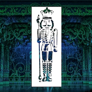 May include: A white stencil of a traditional nutcracker soldier. The stencil is in the shape of a tall, thin man with a crown, a mustache, and a rifle. The stencil is on a blue and green background.