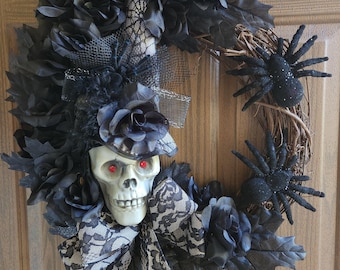 May include: A black and white Halloween wreath with a skull wearing a witch's hat, black roses, and black spiders.