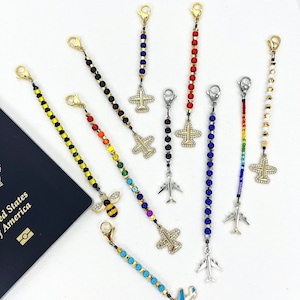 May include: Assortment of colourful beaded luggage tags with airplane charms. The tags feature various colours, including red, blue, yellow, black, white, and rainbow. Some tags have a bee charm instead of an airplane.