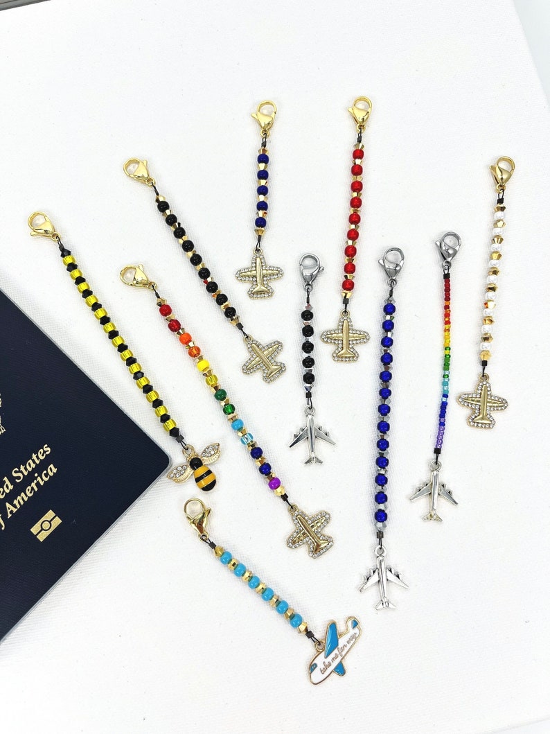 May include: Assortment of colourful beaded luggage tags with airplane charms. The tags feature various colours, including red, blue, yellow, black, white, and rainbow. Some tags have a bee charm instead of an airplane.