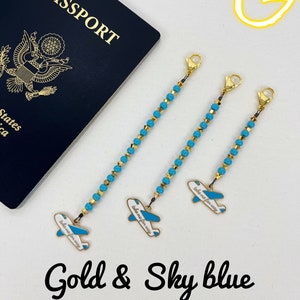 May include: Three gold and sky blue beaded chains with airplane charms. Each charm has the text "take me for a way" on it. The chains are hanging from a white surface. The words "Gold & Sky blue" are written below the chains.