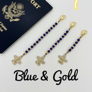 May include: Three gold airplane luggage tags with blue beads and gold clasps. The tags are on a white surface with a blue passport in the background. The text "Blue & Gold" is written below the tags.