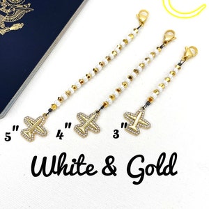 May include: Three gold airplane charms with white beads on a chain. The charms are 3 inches, 4 inches, and 5 inches long. White & Gold text is below the charms.