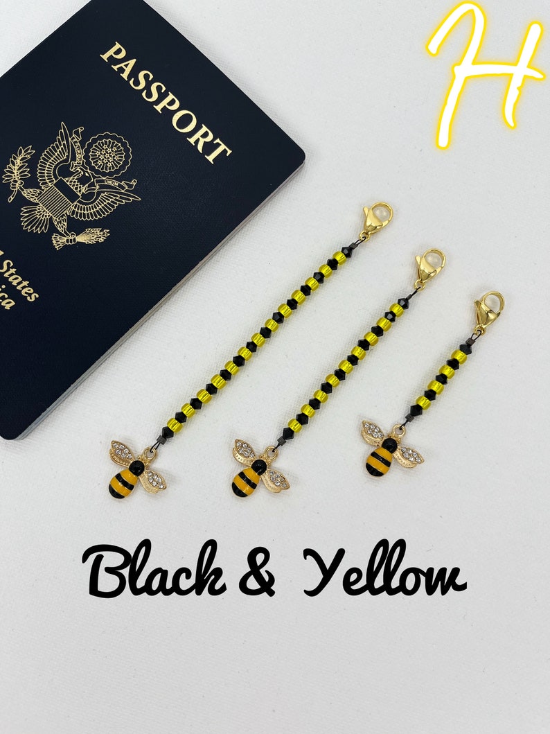 May include: Three black and yellow beaded chains with a gold bee charm at the end. The chains are hanging from a white surface. The text "Black & Yellow" is written below the chains.