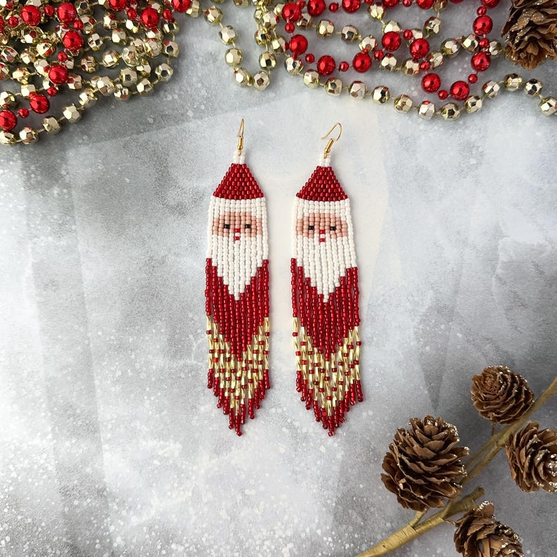 May include: Red, white, and gold beaded earrings with a Santa Claus face design. The earrings are long and dangle.