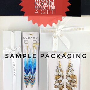 Puede incluir: Dos pares de pendientes de cuentas en cajas blancas con el nombre de la marca "LUBARO" impreso en ellas. Los pendientes est&aacute;n empaquetados en cajas blancas con una cinta blanca. El texto "YOUR EARRINGS WILL COME NICELY PACKAGED! PERFECT FOR A GIFT!" est&aacute; impreso en rojo sobre un fondo blanco.