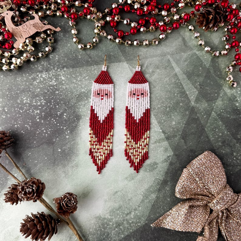 May include: A pair of long, beaded earrings featuring a Santa Claus design. The earrings are red, white, and gold with a fringe of beads.