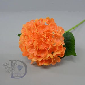 Pode incluir: Uma vibrante flor de hortênsia artificial laranja com um caule e folha verdes. A cabeça da flor é um grupo redondo e completo de pequenas flores em forma de pétalas. O caule é longo e fino, e a folha é verde escuro. Um item decorativo.