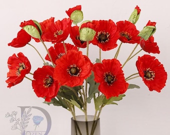 May include: A bouquet of vibrant red poppy flowers with dark centers and green stems and leaves. The poppies are arranged in a clear glass vase, creating a striking floral display. The image showcases the beauty of the flowers.