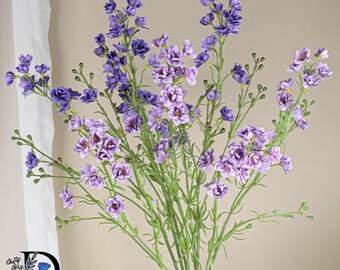 May include: A bouquet of artificial flowers featuring multiple stems with small, delicate blossoms in shades of deep purple, lavender, and light violet. The flowers are arranged on thin green stalks with small, round, unopened green buds.