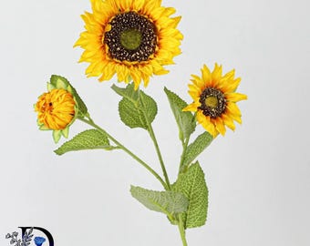 May include: A decorative artificial sunflower stem featuring one large fully bloomed yellow flower, one smaller partially opened yellow flower, and one closed yellow bud. The stem includes several textured green leaves with visible veins.