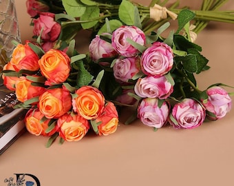 May include: A collection of artificial rose bouquets featuring vibrant orange and soft pink petals. Each stem includes green leaves and buds, bundled together with twine. The flowers display layered, rounded blooms with realistic textures and stems.