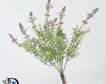 May include: A faux lavender plant stem featuring multiple branching green stalks with narrow leaves and small, light purple flower spikes at the tips. The plant has a textured, realistic appearance with a central stem base and a logo in the corner.