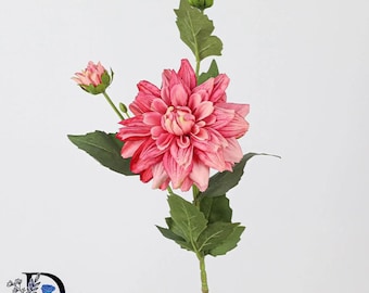 May include: A single artificial dahlia stem featuring one large, multi-petaled pink flower, two smaller unopened buds, and several green leaves on a slender stalk. The petals display a gradient of pink tones, and the stem includes a logo.