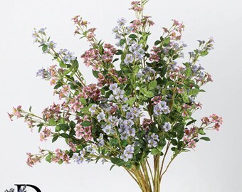 May include: A bouquet of artificial flowers featuring small, delicate blossoms in shades of dusty pink and light periwinkle blue. The stems are thin and brown, adorned with numerous small, pointed green leaves distributed along the branching stalks.