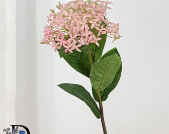 May include: A single artificial stem featuring a cluster of small, light pink four-petaled flowers arranged in a rounded head. The stem includes several dark green, oval-shaped leaves with visible veins and a brown, textured stalk extending downward.
