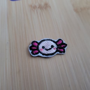 May include: A pink and black embroidered axolotl patch with a smiling face.