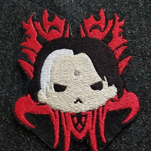 May include: Black and red embroidered patch featuring a cartoon character with white skin, black hair, and a red and black design. The character has a serious expression and a small, pointed nose.