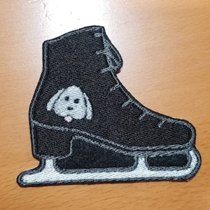 Puede incluir: Parche de hierro bordado negro de un patín de hielo con un pequeño perro blanco en el lateral.