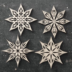 May include: Four laser-cut wooden snowflakes with intricate designs. The snowflakes are arranged in a square pattern on a dark gray background.