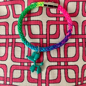 May include: A rainbow colored braided bracelet with a silver clasp and a teal balloon dog charm.