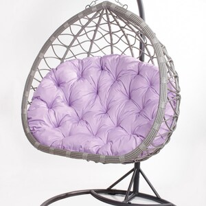 May include: A gray wicker egg chair with a lavender tufted cushion. The chair hangs from a black metal stand with a circular base. The chair is designed for outdoor or indoor relaxation.